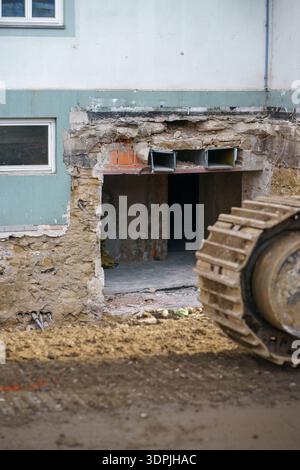 Macchinari pesanti smantellamento della facciata danneggiata dell'edificio residenziale durante i lavori di ristrutturazione, cantiere con detriti e struttura esposta. Foto Stock