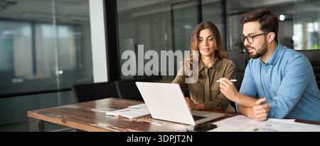 Due colleghi impegnati che lavorano insieme parlando utilizzando un notebook in ufficio. Foto Stock