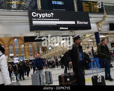 Stazione di Liverpool Street, LONDRA, Regno Unito. 13 febbraio 2026. I pendolari passano davanti a uno schermo pubblicitario digitale da JCDecaux in una stazione ferroviaria principale di Londra. Sullo schermo viene visualizzato un annuncio per bitwise Asset Management, un gestore globale di risorse per criptovalute che mette in evidenza le sue soluzioni di investimento in asset digitali. Foto Stock