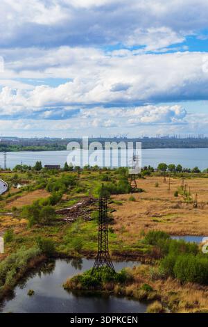Un paesaggio pittoresco con una linea elettrica accanto a un lago e un bel cielo nuvoloso Foto Stock