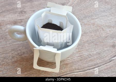 gocciolatoio di caffè in polvere con filtro e cucchiaio di legno nel bicchiere da tazza sul tavolo Foto Stock