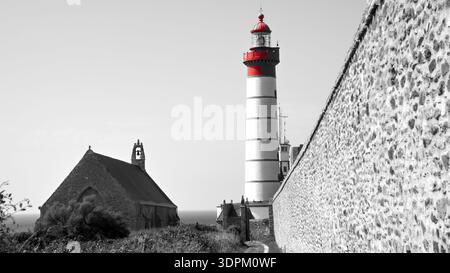 Un'impressionante fotografia in bianco e nero con un solo faro rosso in piedi in un aspro paesaggio costiero roccioso. Foto Stock