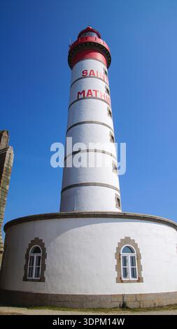 Un torreggiante faro a righe rosse e bianche con finestre ad arco decorative si innalza su di un cielo blu limpido, che mostra l'eleganza architettonica marittima. Foto Stock