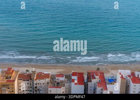 Appartamenti lungo la tranquilla costa turchese. Alloggi con luce mattutina e acque tranquille. Le case rigogliose si affacciano sul mare calmo all'alba Foto Stock