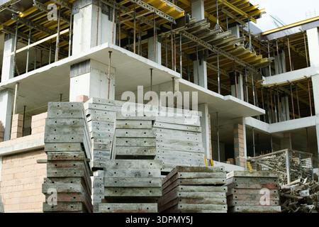 Costruzione di edifici in cemento armato con colonne, lastre, impalcature e pannelli per casseforme impilati in cantiere. Foto Stock