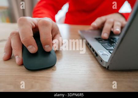 Primo piano di un mans mano che fa clic sul mouse di un computer mentre l'altra mano digita sulla tastiera di un notebook. Ambiente di lavoro domestico o di ufficio. Concetto di telecomando Foto Stock