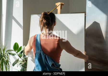 Artista donna concentrata nel processo creativo in officina, preparando tela per dipingere un nuovo quadro. Foto Stock