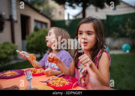 I bambini mangiano pasta all'aperto durante la cena estiva sul cortile Foto Stock
