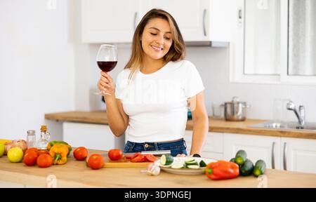 Sorridente giovane ispanica che cucina e beve vino a casa Foto Stock
