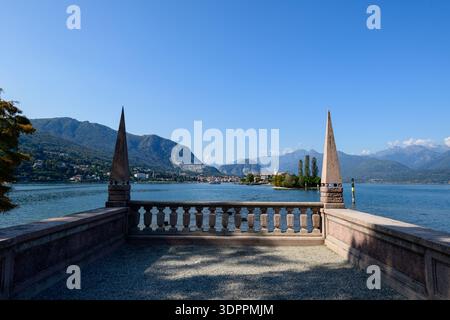 Isola bella, Italia - 30 settembre 2020: Una terrazza in pietra con balaustra e due obelischi appuntiti si affaccia sul Lago maggiore, con l'Isola dei pescatori e le lontane montagne visibili sotto un cielo azzurro. Foto Stock