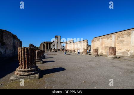 Pompei, Italia - 4 ottobre 2020: L'immagine mostra un'ampia vista delle antiche rovine della basilica di Pompei, con file di colonne in mattoni, pareti in pietra parziali e diversi visitatori che camminano attraverso il sito archeologico sotto un cielo azzurro. Foto Stock