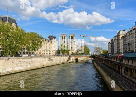 Parigi, Francia - 14 aprile 2022: La cattedrale di Notre-Dame è visibile sullo sfondo con una gru da costruzione accanto, mentre il fiume Senna scorre tra edifici storici e alberi frondosi sotto un cielo parzialmente nuvoloso. Foto Stock