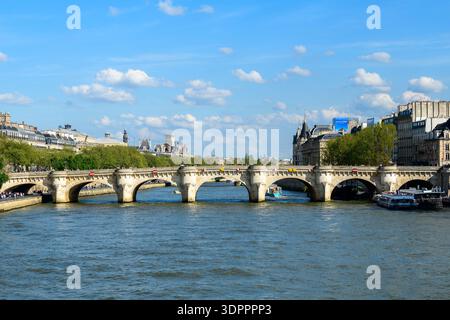 Parigi, Francia - 14 aprile 2022: Il ponte le Pont Neuf attraversa la Senna con le barche che passano sotto e gli edifici storici parigini, tra cui la Conciergerie, visibili lungo le rive del fiume sotto un cielo blu. Foto Stock