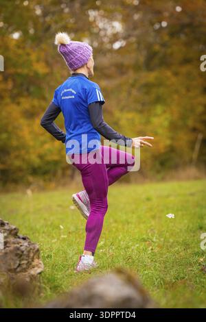 Donna che indossa pantaloni sportivi rosa e giacca blu da allenamento nella foresta autunnale, atleta di media distanza Katharina Jaiser, Gechingen, Germania Foto Stock