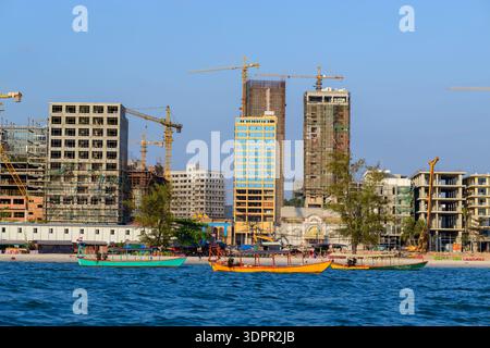 Sihanoukville, Cambogia - 29 gennaio 2020: Numerosi grattacieli e gru sono visibili lungo il lungomare, con diverse barche di legno colorate in primo piano e attività di costruzione in corso sulla costa. Foto Stock