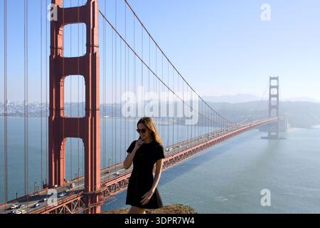 Donna in piedi vicino al Golden Gate Bridge in abito nero Foto Stock