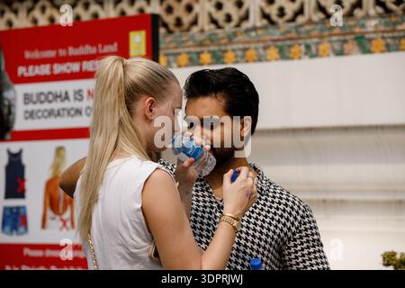 BANGKOK, THAILANDIA - 21 GENNAIO 2026: Coppia turistica in piedi insieme, bere acqua da una bottiglia di plastica, pelle femminile, profilo laterale, a Wat Arun. Foto Stock