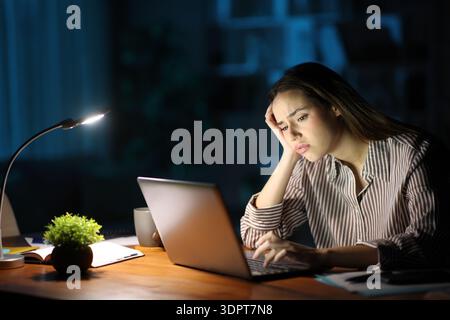 Teletrasporto preoccupato durante la notte di lavoro online controllando il laptop a casa Foto Stock