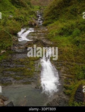 Una vista aerea della cascata di Du Gia che scorre su formazioni rocciose a strati e che si getta in piccole piscine circondate da una lussureggiante vegetazione verde. Foto Stock