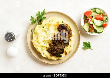 Piatto con fegato, cipolle caramellate e purè di patate con sugo di carne. Sfondo in pietra chiara, vista dall'alto, disposizione piatta Foto Stock