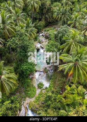 Vista aerea angolata delle Cascate di Inambakan che scorrono attraverso piscine e cascate turchesi, circondate da fitte palme e vegetazione tropicale. Foto Stock