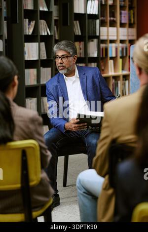 Uomo dell'Asia meridionale di mezza età che dà una presentazione con il libro a un pubblico diverso Foto Stock