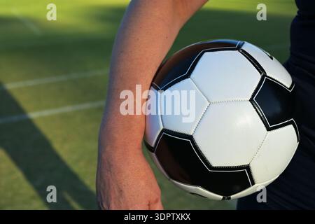 Primo piano di una persona che tiene una palla da calcio bianca e nera su un campo di erba durante le attività sportive all'aperto Foto Stock