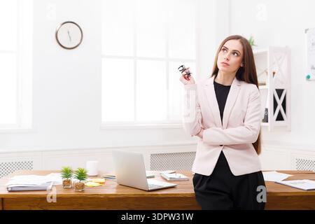 Donna professionista che pensa in un ambiente ufficio con un notebook e documenti sulla scrivania Foto Stock