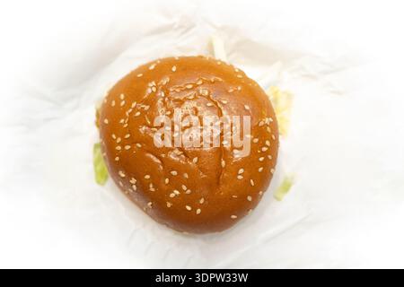 Vista dall'alto verso il basso di un panino di hamburger con semi di sesamo su carta bianca, che rivela parzialmente la lattuga sotto, sfondo isolato Foto Stock