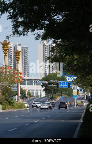 Strada urbana con edifici moderni e alti, flusso di traffico, statue dorate e viale alberato sotto il cielo limpido Foto Stock