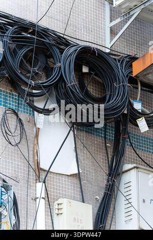 Cavi elettrici neri avvolti e aggrovigliati su una parete piastrellata con cassette di servizio in ambiente urbano Foto Stock