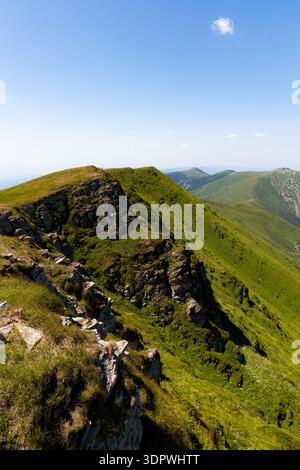 Vista di una cresta di montagna verdeggiante sotto un cielo azzurro, il terreno accidentato un arazzo di verde e marrone, coinvolgente avventura, Bela Palanka, Pirotski Foto Stock