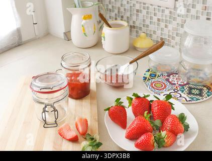 Composizione di fragole fresche e vasetti vuoti in cucina. Prodotti agricoli di stagione e conserve fatte in casa. Crea sfondo. Foto Stock