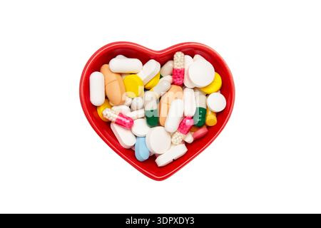 Ciotola a forma di cuore con un assortimento colorato di vari integratori isolati su sfondo bianco. Foto Stock