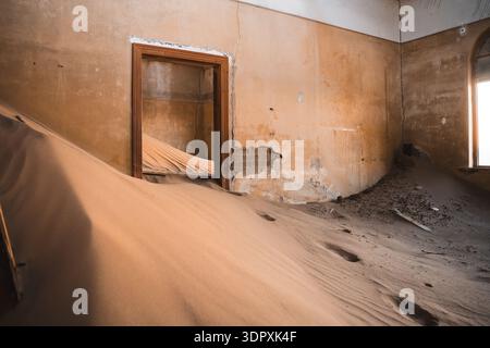 Le dune di sabbia illuminate dal sole riempiono un interno abbandonato nella città fantasma di Luderitz, mostrando l'affascinante miscela di architettura e natura nel deserto del Namib Foto Stock