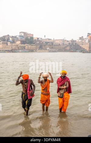 Tre sadhus indù in tradizionale abbigliamento arancione eseguono rituali nel fiume Gange a Varanasi, in India. Foto Stock