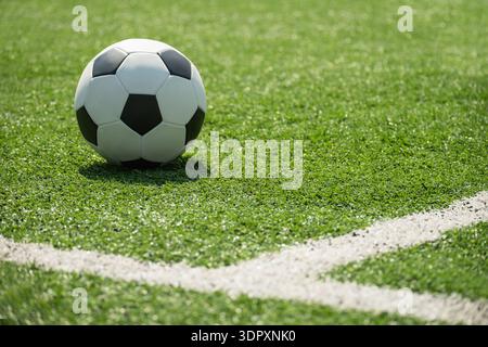 Classico pallone da calcio su erba sintetica verde vicino alla linea d'angolo sul campo da calcio, sfondo sportivo con spazio fotocopie Foto Stock