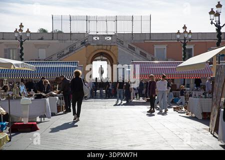 Mercato delle pulci a Nizza, nel sud della Francia, con bancarelle a righe, curiosando tra gli acquirenti e l'architettura storica sotto la chiara luce mediterranea. Foto Stock