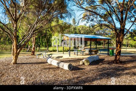 Area picnic del parco con padiglione coperto, panche di tronchi e alberi ombreggiati sotto il cielo luminoso nella riserva dei laghi Piney, Perth, Australia, 16 dicembre 2020 Foto Stock