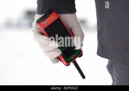 Un walkie-talkie con custodia protettiva arancione in mano a un lavoratore in un guanto bianco. Foto Stock
