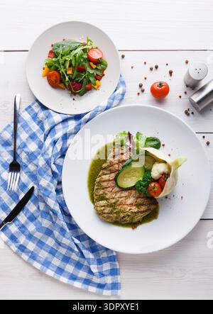 Pesce alla griglia con insalata servito su un piatto con tovagliolo a scacchi blu al tavolo Foto Stock