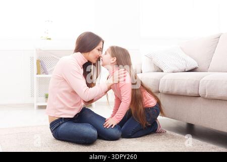 Madre e figlia condividono un momento a casa con espressioni gioiose e una stretta interazione Foto Stock