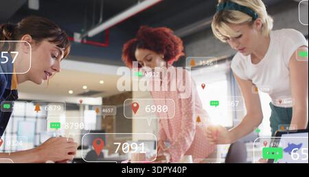 Tre donne che lavorano in blu-rosa-verde appoggiate al tavolo dell'ufficio, utilizzando un computer portatile con icone AR Foto Stock