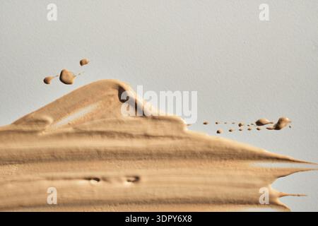 Campione cosmetico con fondo liquido beige che mostra una consistenza cremosa su sfondo chiaro Foto Stock
