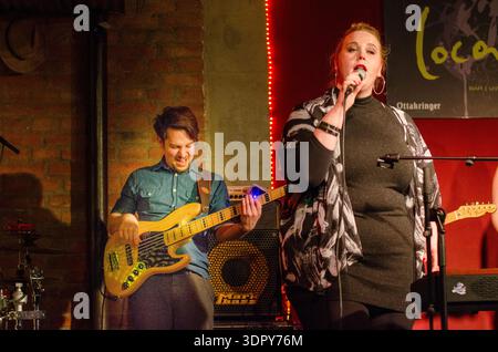 Presentazione Babsea CD cantante femminile con microfono in mano si esibisce sul palco accanto al bassista maschile; luci calde da club Foto Stock
