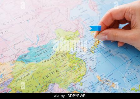 Scegliere una posizione su una mappa dell'Asia con una bandiera blu in mano Foto Stock