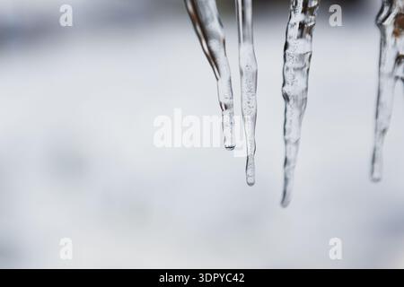 I ghiaccioli sono appesi da un tetto in una fredda giornata invernale vicino a un paesaggio innevato Foto Stock