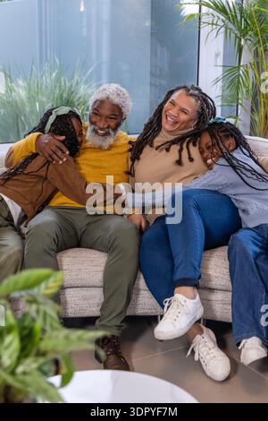 Famiglia afroamericana che si coccola sul divano di casa, senior che abbraccia due bambine al tavolino da caffè Foto Stock