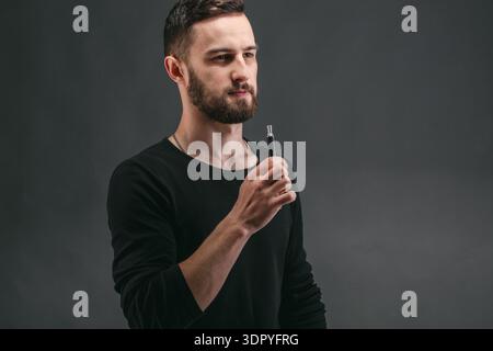 Man tiene il dispositivo Vaping in un'impostazione Studio con sfondo scuro durante una sessione interna Foto Stock