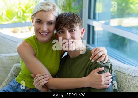 Madre e figlio adolescente seduti sul divano accanto a grandi finestre madre che indossa la parte superiore verde e l'anello Foto Stock